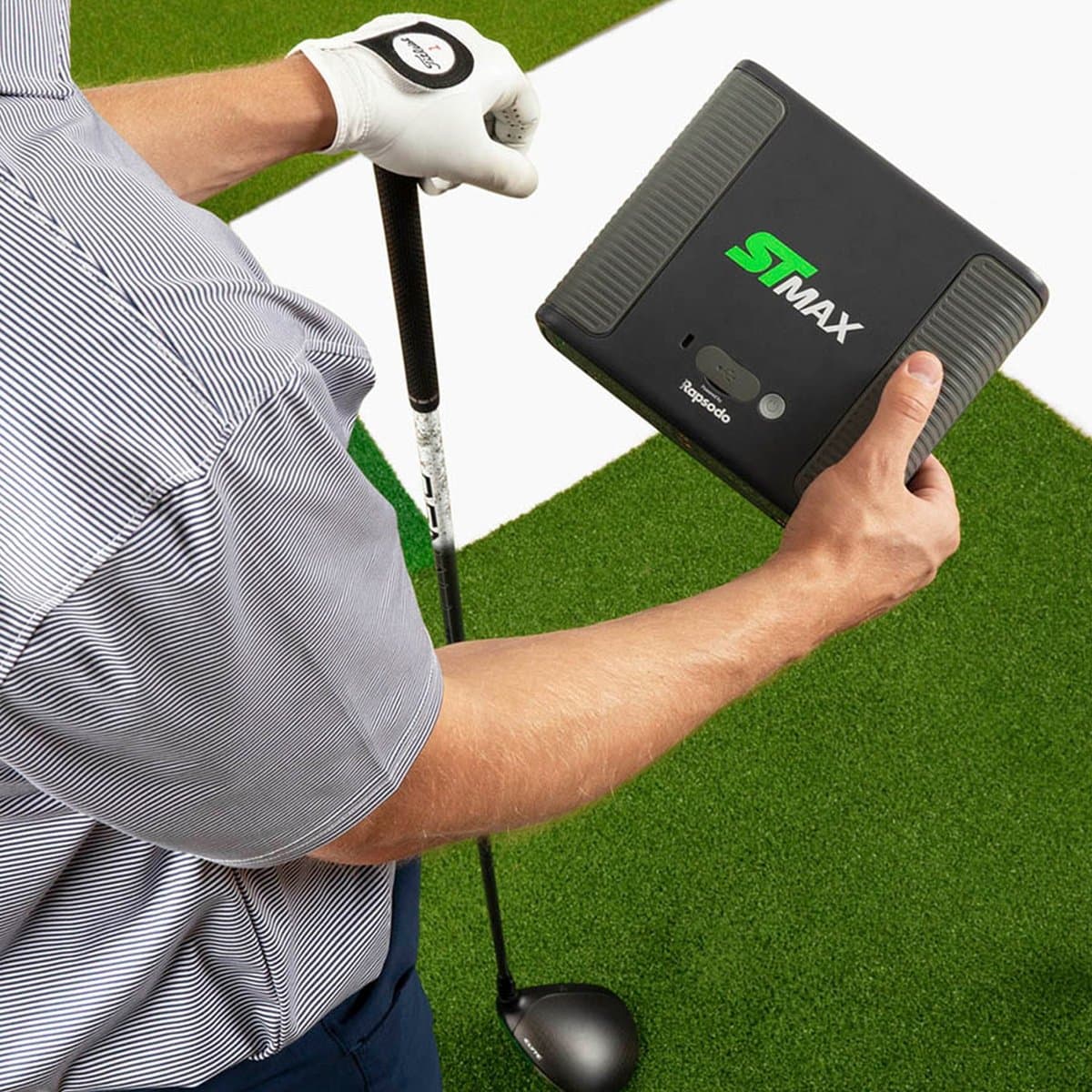 SkyTrak+ launch monitor positioned on golf mat with golfer mid-swing and wall-mounted display showing ball flight