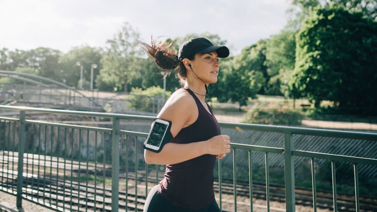Runner wearing open-ear headphones on a city street with traffic visible in background