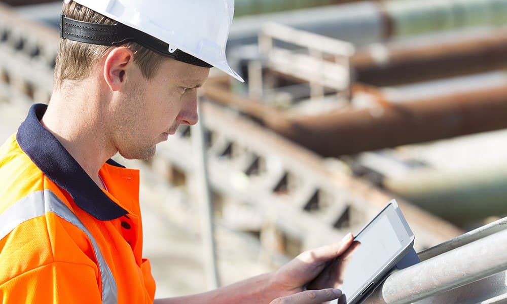 Construction worker using rugged smartphone on job site with concrete and steel beams in background